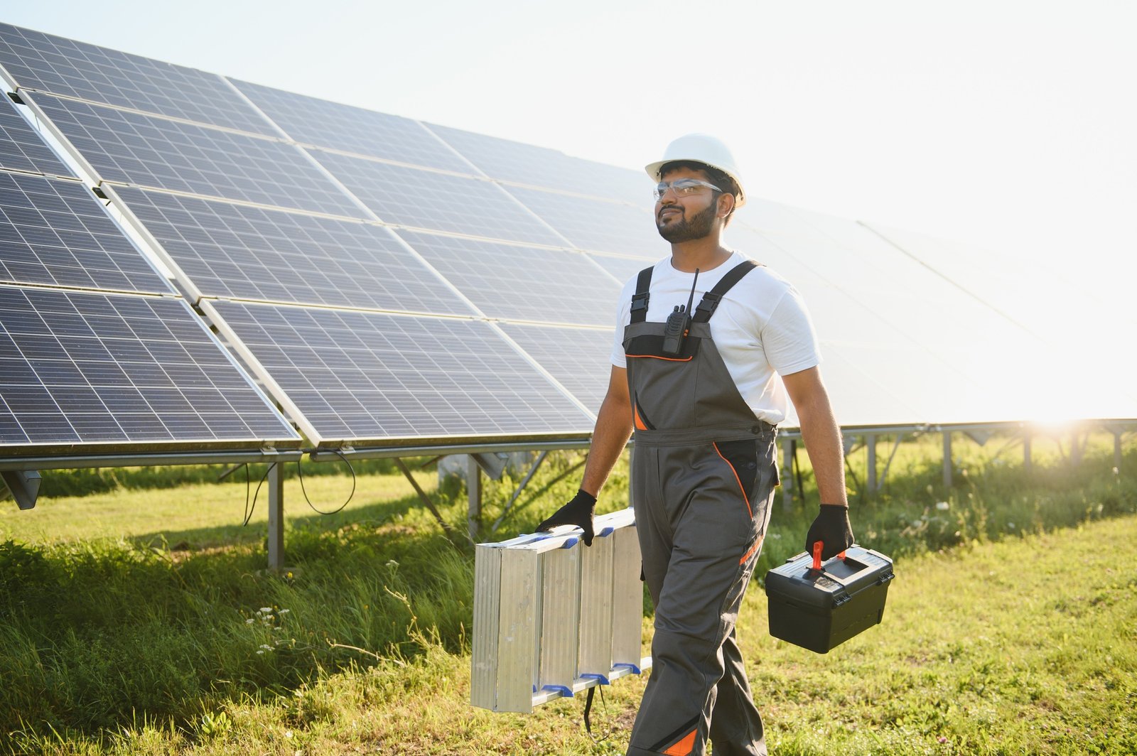 An Indian worker in uniform and with tools works on a solar panel farm
